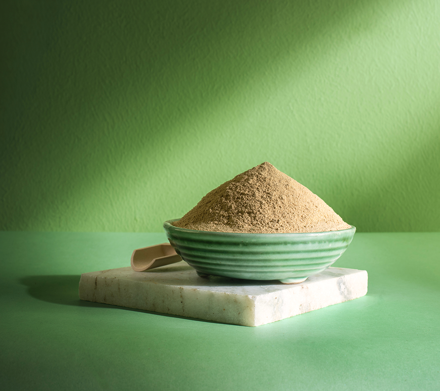 A bowl of ubtan powder on a marble slab against a green wall.